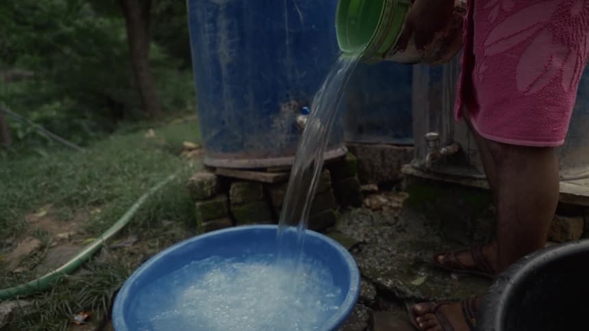 Person pours water from a container into a blue basin next to a reservoir and taps