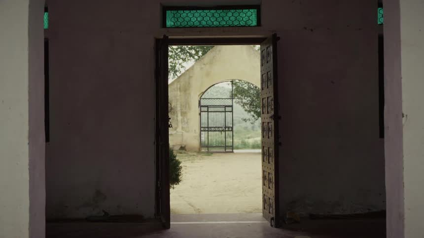 Open doorway reveals an outdoor courtyard with an arch and metal gate in the distance
