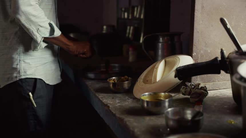 Person preparing food on modest kitchen counter with metal utensils and soft lighting