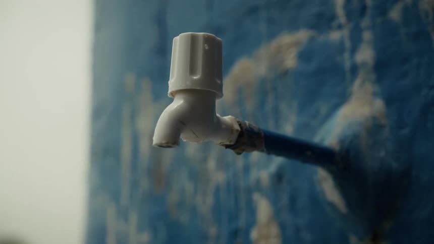 White plastic faucet protrudes from a weathered blue wall