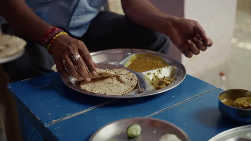 Hands serve food with flatbreads on steel plates atop a blue table