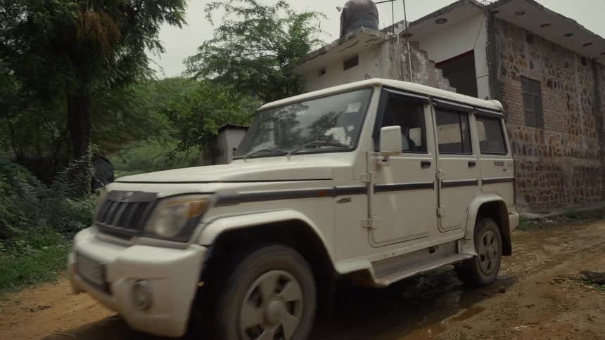 An suv drives along an untarred street passing a building in a developing community