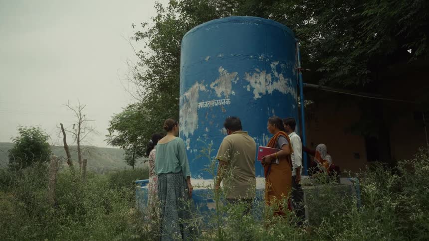 Group of people examine a large weathered blue tank in an overgrown area