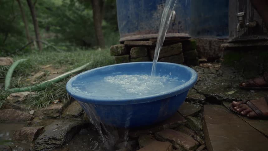 Stream of water fills a blue basin placed on the damp ground