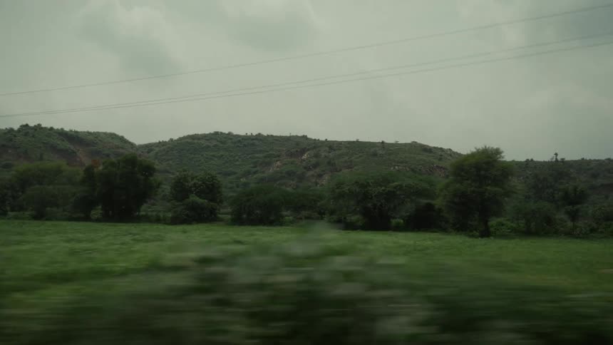 A landscape of green hills filled with trees in the foreground seen from a moving image