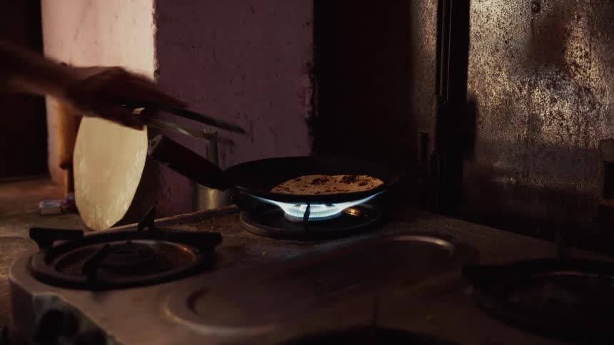 Roti cooks over a blue flame as a hand holds the pan on the stove