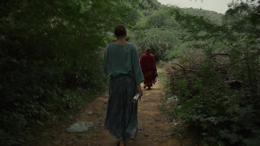 Woman walks along a dirt path surrounded by dense vegetation