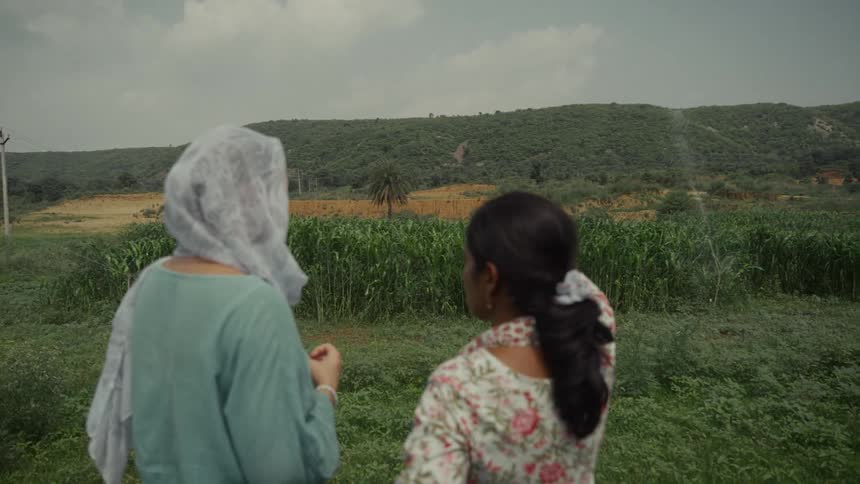 Two women look out over green crops toward vegetationcovered hills