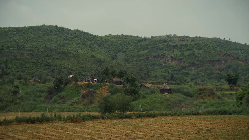 Small huts are scattered among green hills and dense vegetation