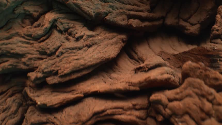 The video is a slow detailed closeup pan across a piece of highly textured gnarled driftwood or an abstract wooden sculpture the rich brown surface features deep grooves and rough organic ridges giving it a dramatic mountainous appearance against a