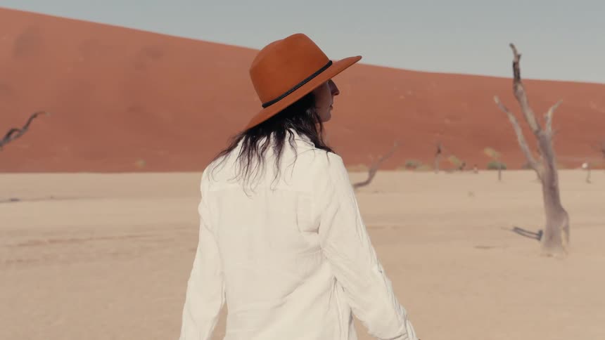A woman wearing a hat walks through a dry desert landscape