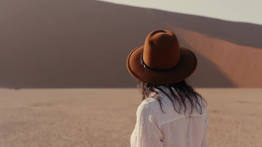 Woman wearing a sunhat turns her head looking at desert dunes