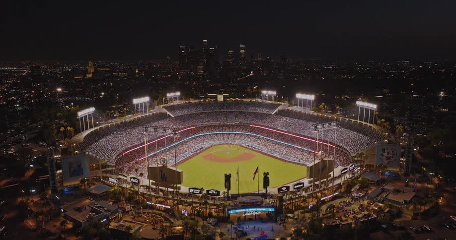 A wideangle aerial shot of dodger stadium in los angeles californiaat night during a baseball game the stadium is brightly illuminated with field lights showing the green playing field and stands set against the backdrop of los angeles
