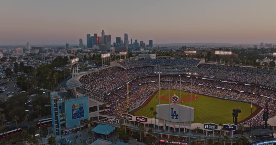 Dodger stadium packed at sunset with game in progress and city skyline in the background