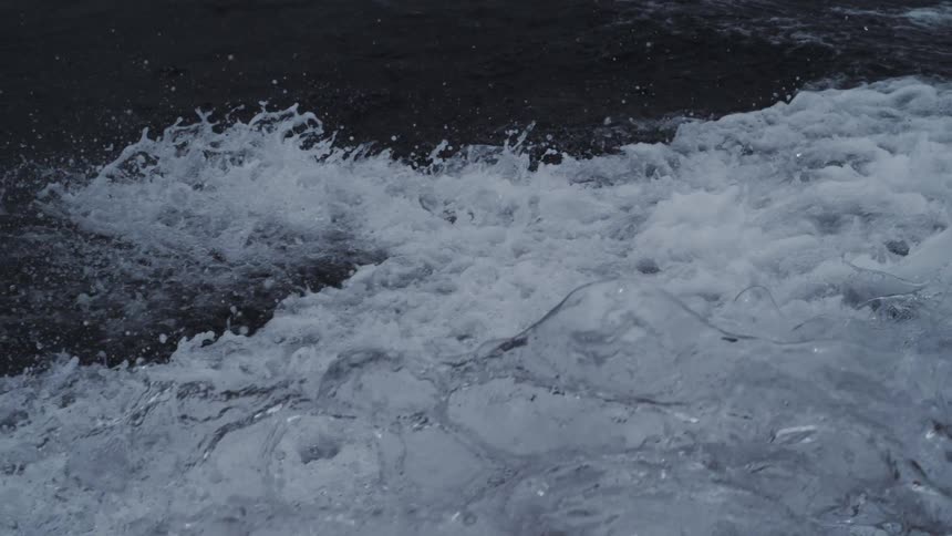 Churning white foam and water spray splash against the dark surface of the ocean