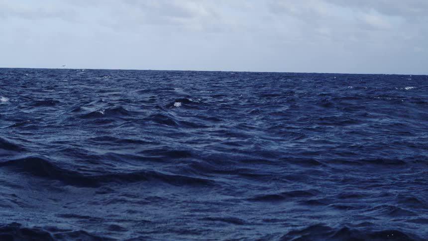 Dark blue ocean surface with moderate waves under partly cloudy sky