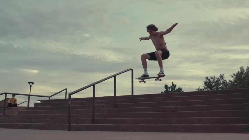 A shirtless skateboarder performs a jump down a set of stairs