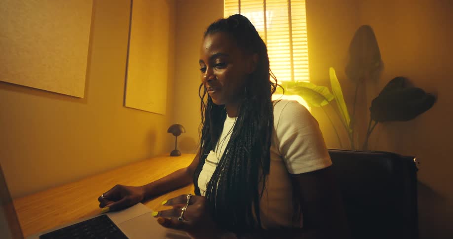 A woman is in a room with yellow light while sitting and using a laptop