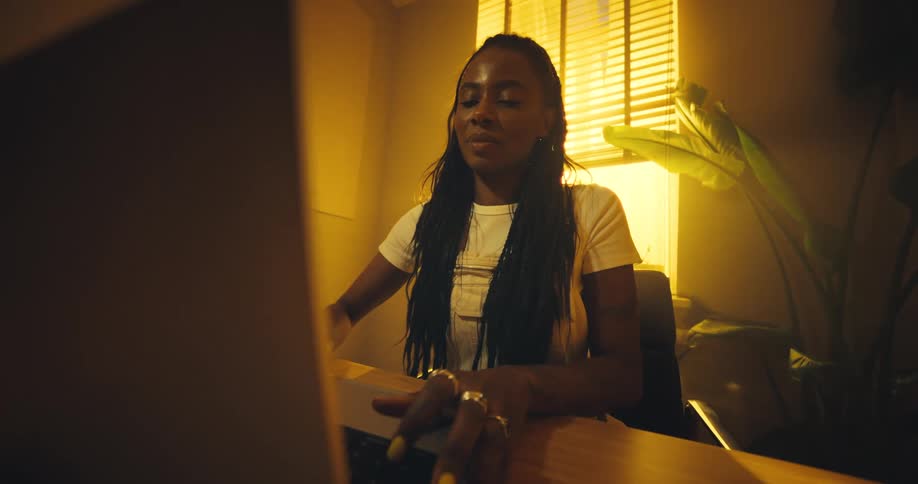 A woman sits at her desk opens her laptop with a smile and prepares to work as warm golden light fills the room