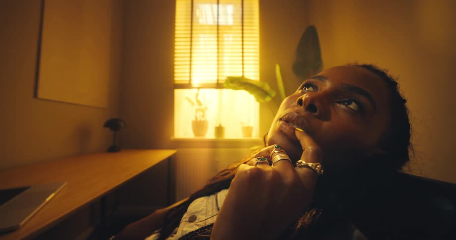 A woman sits at a desk gazing upward thoughtfully in a warm low lit office