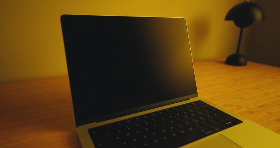 Laptop computer sitting on a table with a lamp near the wall