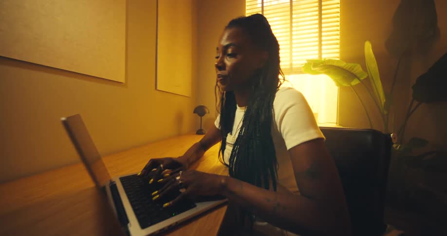 As the view draws closer a focused woman begins typing on her laptop her face illuminated by the warm glow of a nearby window