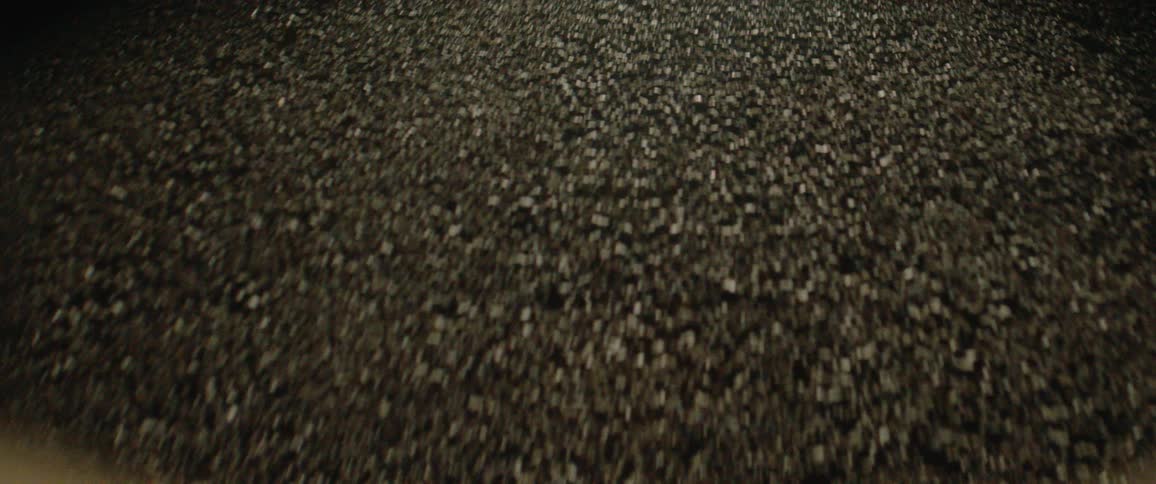 The video shows a closeup lowangle shot of a surface covered in dark small uneven gravellike stones or pebbles the surface moves slightly away from the camera suggesting motion over the ground