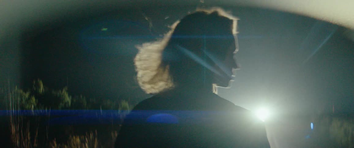 A woman with her back turned is walking forward outdoors at night towards a spotlight