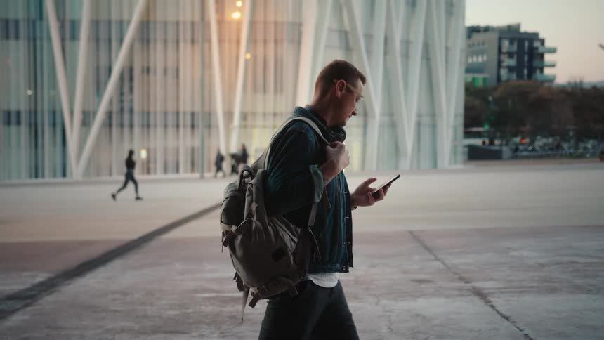 The man looks at his phone while walking through the city