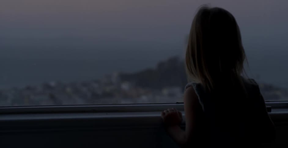 A little girl looks out of a window overlooking a city