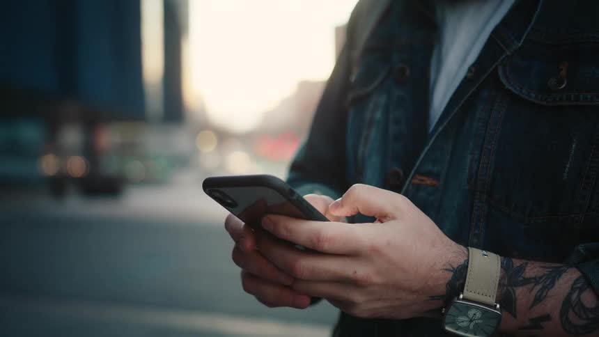 Person with forearm tattoo using phone on city street