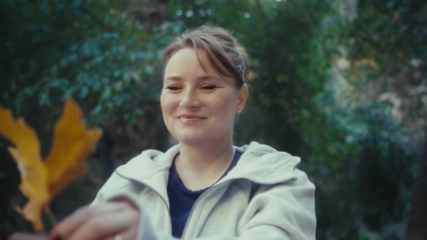 A smiling woman holds up a yellow leaf and uses her smartphone to take a picture of it