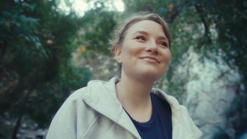 A woman is sitting on a rock outdoors and has a small smile on her face