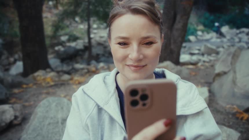 Woman holds her phone as she takes a picture of a leaf in her hand