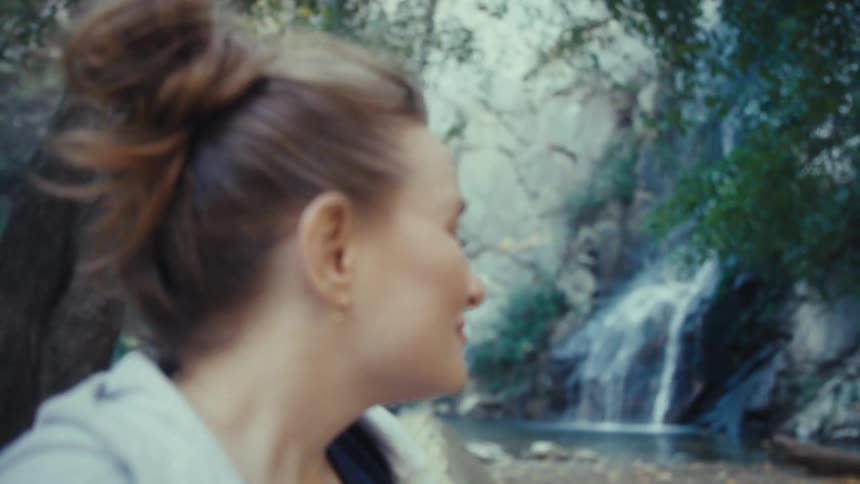The video features a closeup profile shot of a woman with her hair in a bun initially smiling with her eyes closed as she enjoys the natural surroundingsshe then opens her eyes and slowly turns her head to look toward the background which is reveal