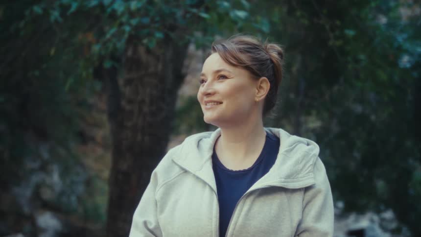 A woman stands smiling in a lush forest enjoying the peaceful surroundings