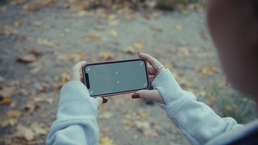 A persons hand wearing gray coat sleeves holding a cell phone with a completely black screen