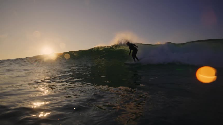 Surfer in silhouette gliding on wave lit by sunset