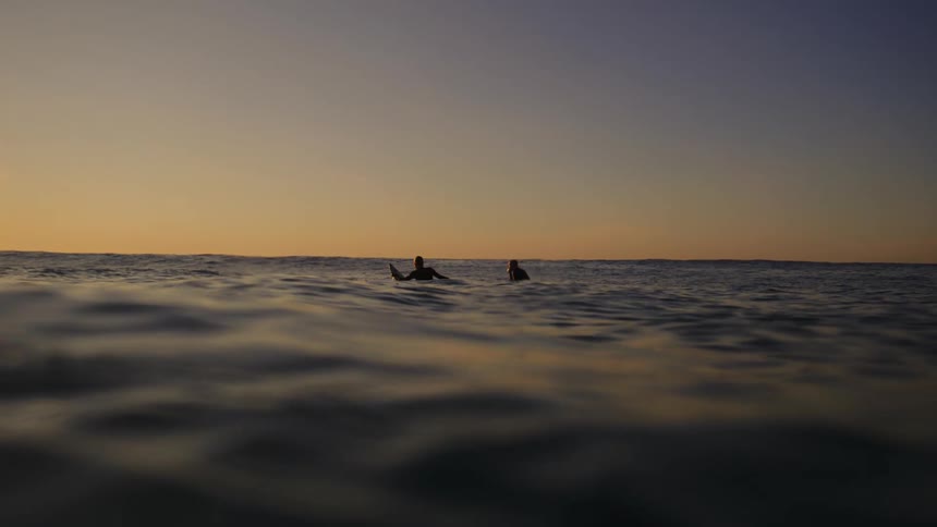 Two people watch the sun rise while floating on their surfboards