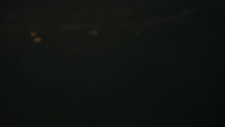 A solitary mans silhouette is looking forward submerged to the chest in water on a surfboard with intense sun flares at sunset