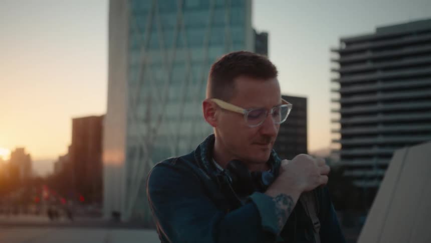 Man wearing glasses walking on the terrace of a building in a metropolitan area while looking at a smartphone in his hand outdoors during day time