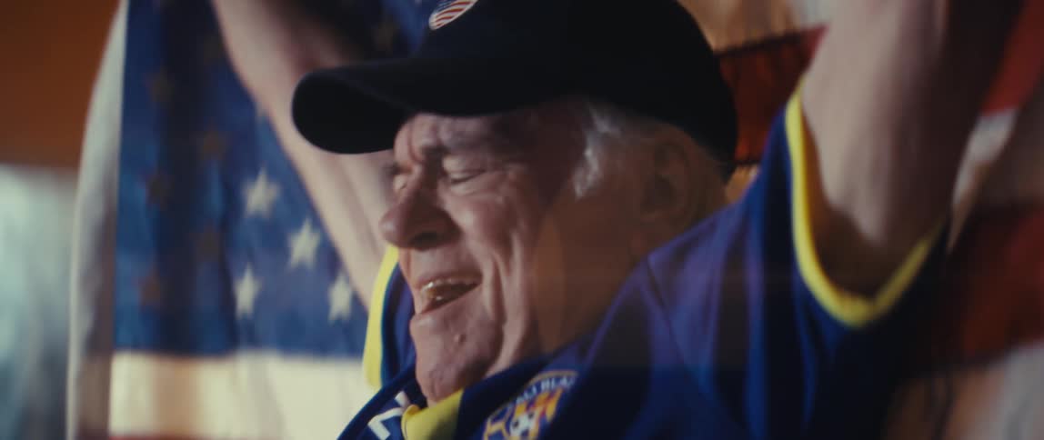Elderly man in blue sports jersey cheering in front of united states flag