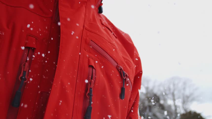 Person wearing a red jacket standing under a snowstorm and moving their hand downwards in a gesture outdoors during day time