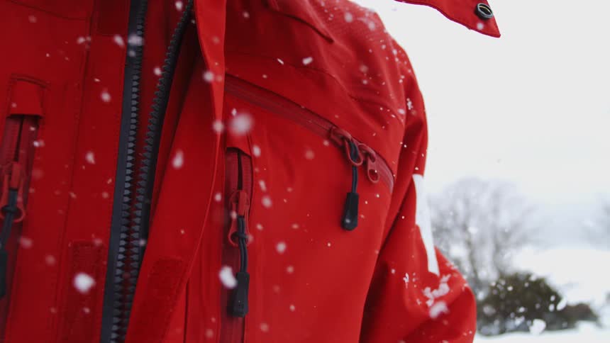Red jacket with snow buildup in outdoor setting with trees and covered ground
