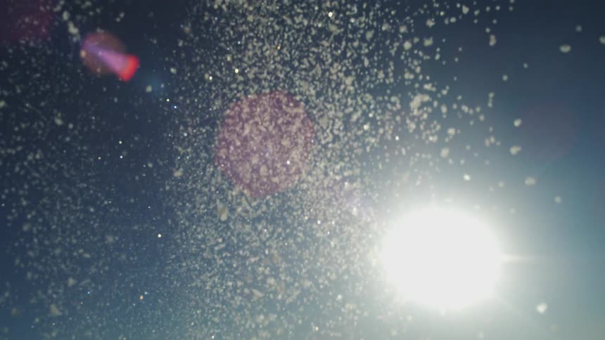 Snow sparkles as it falls from above as the sun shines brightly in a clear blue sky