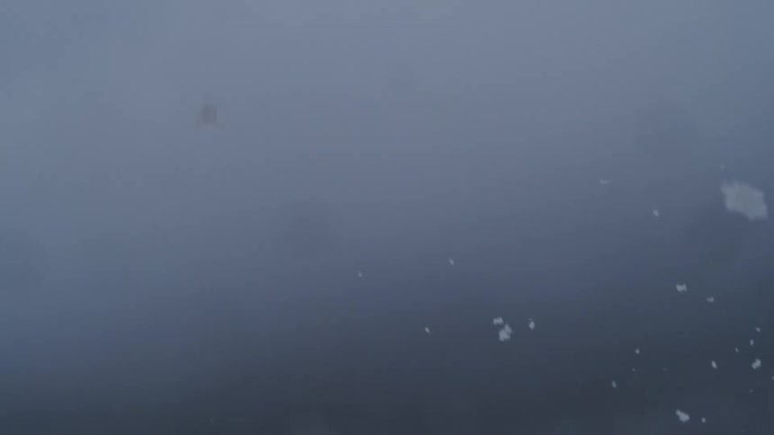 Fast snowfall on a barely visible mountain area covered on dense fog