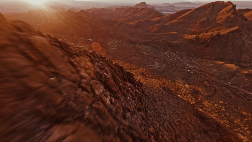 An aerial view captures a steep rocky mountain ridge stretching into the distance under the warm bright setting or rising sun bathing the arid landscape in an intense orange glow