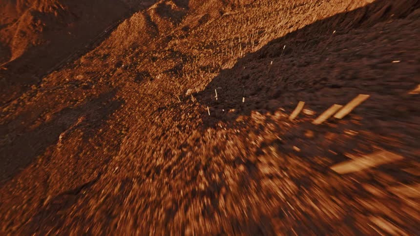 This is a fastmoving downward aerial shot over a steep rocky reddishbrown desert landscape possibly filmed by a drone as the camera flies lower and pulls back slightly the terrain reveals numerous tall columnar cacti growing vertically along the