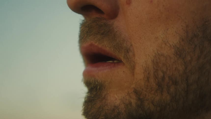 Man with a beard and mustache stands outdoors smoking