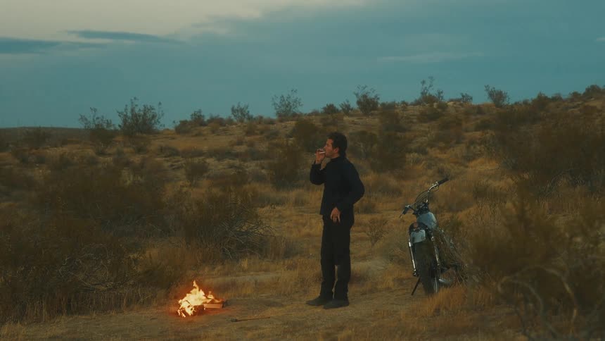 The man is smoking a cigarette by the camp fire